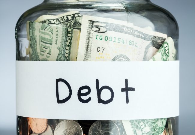 Immagine di un barattolo con dentro delle monete e un foglio con scritto "Debt"