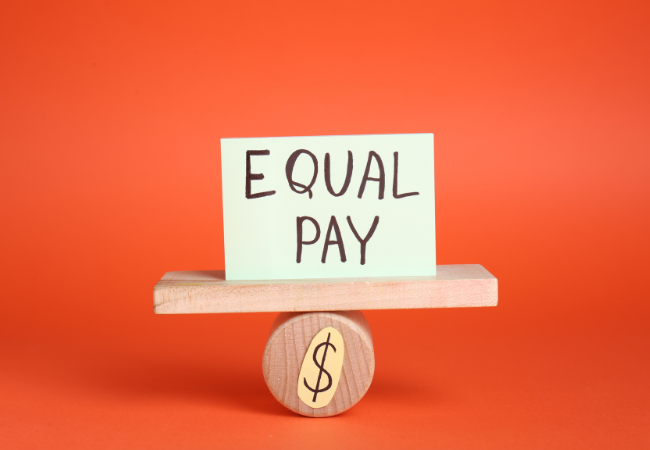 immagine di foglio di carta con su scritto "parità salariale" su un'altalena in miniatura