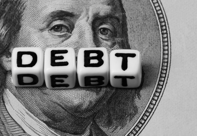 Immagine di alcuni dadi sopra un dollaro che formano la parola "DEBT".