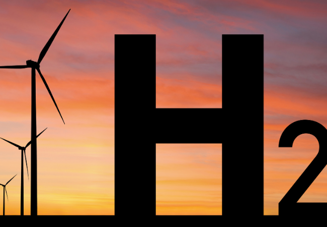 immagine di sagoma in 3d di H2 davanti a delle turbine eoliche al tramonto