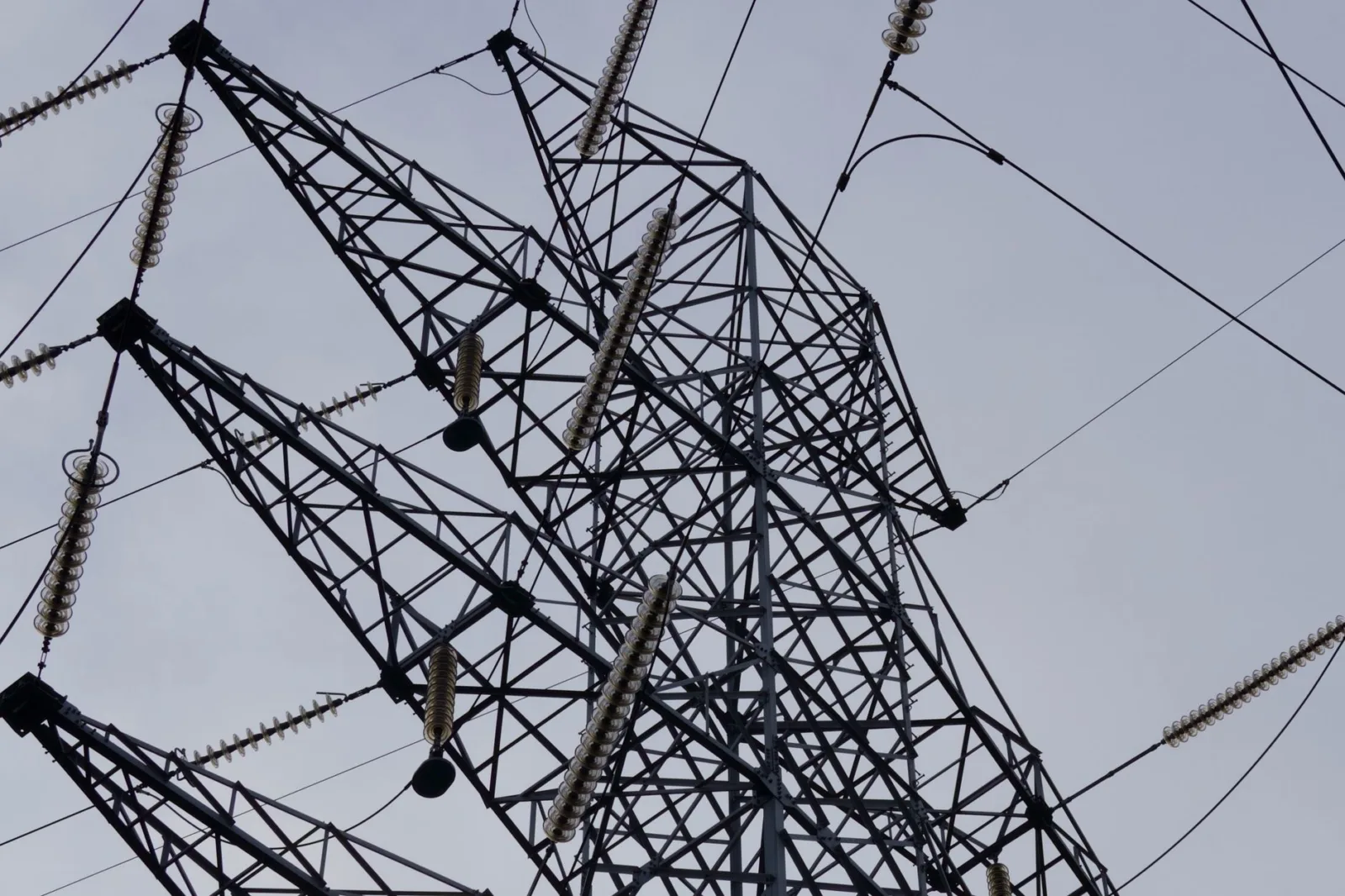 Low angle shot of a metal power transmission tower with cables against a clear sky.