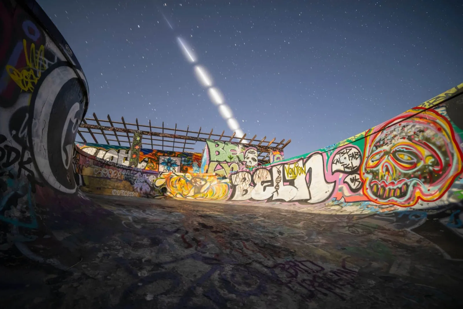 Dynamic view of a graffiti-covered skate park under a starry night sky with light trails.