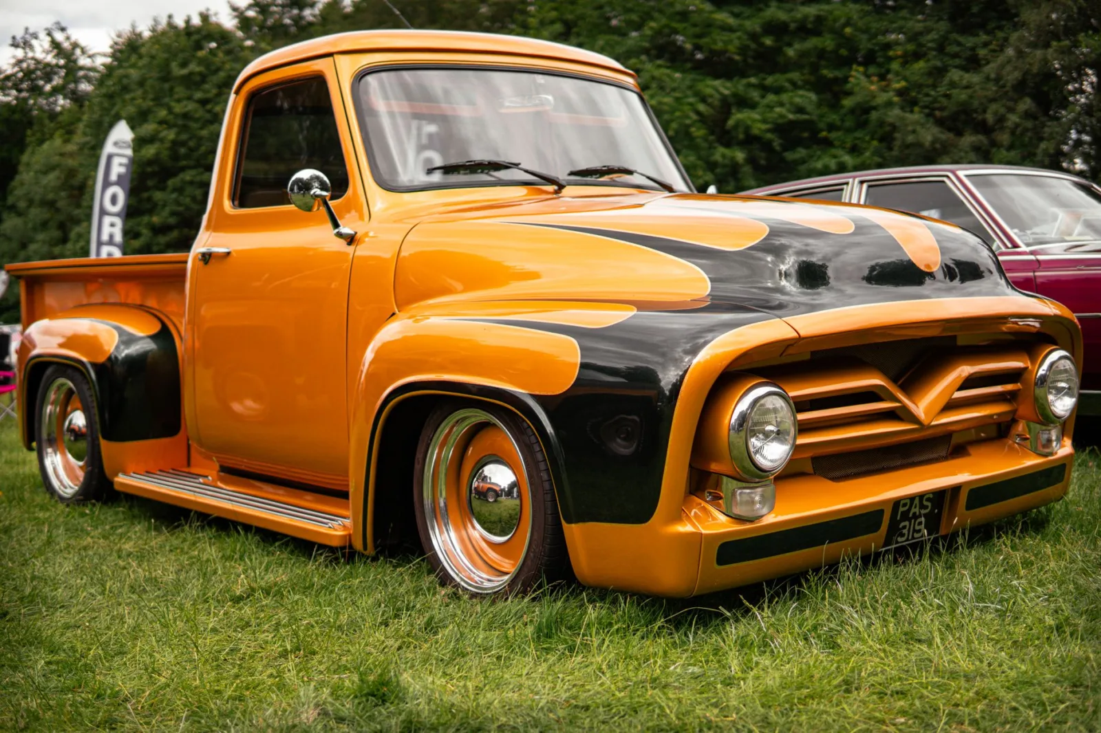 Classic orange Ford pickup truck with custom paint job parked outdoors on green grass.