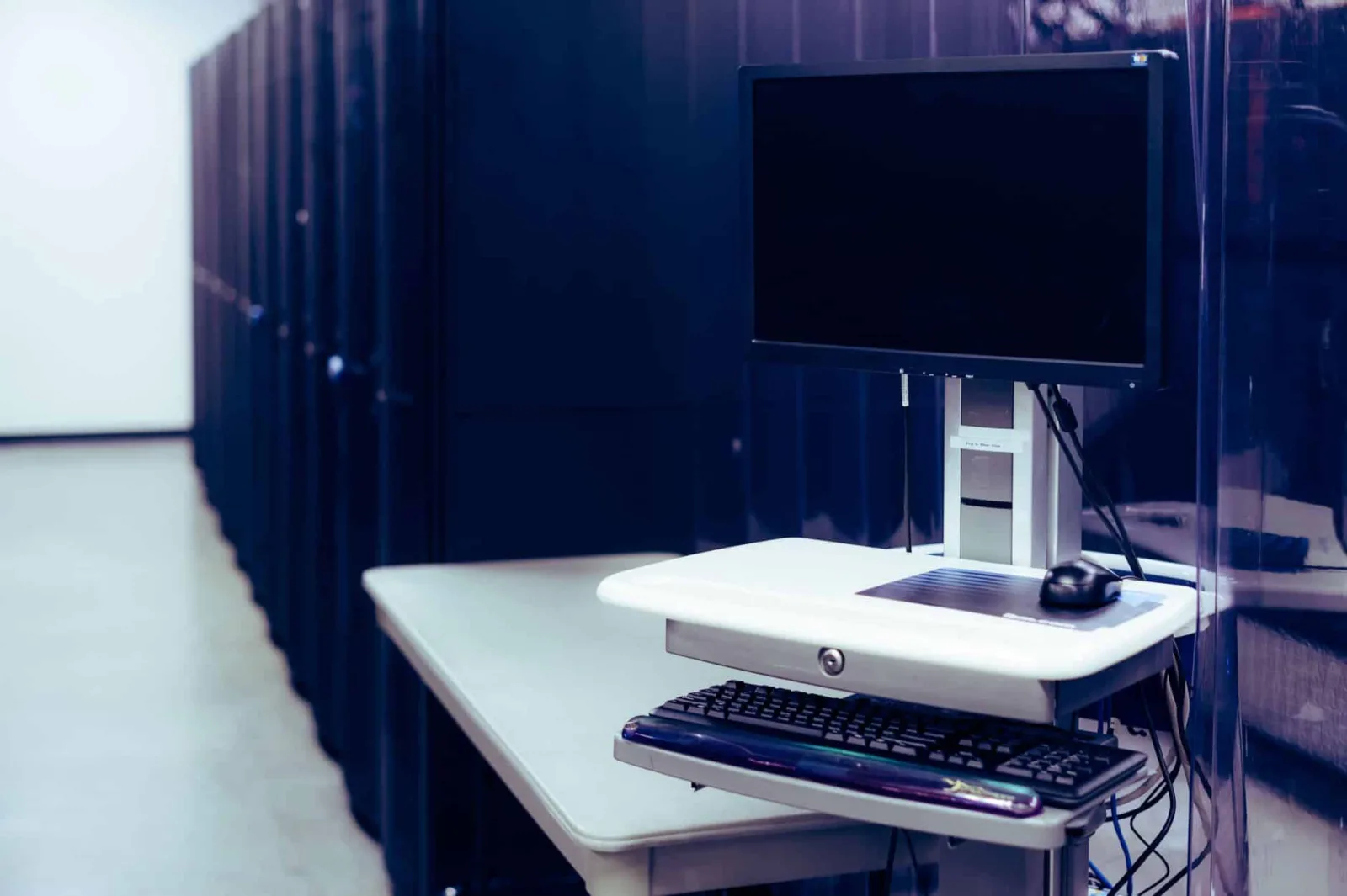 Contemporary computer with black screen placed on stand near row of server steel racks in data center