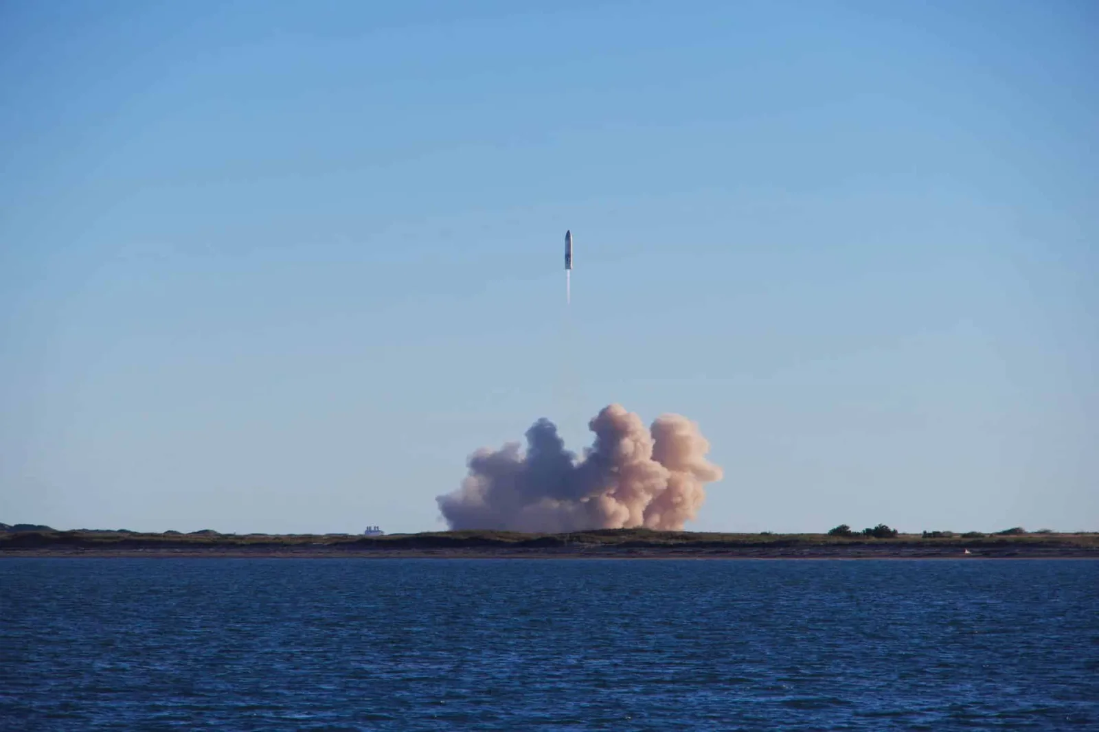 A rocket launch with smoke trails over South Padre Island, viewed across the ocean.