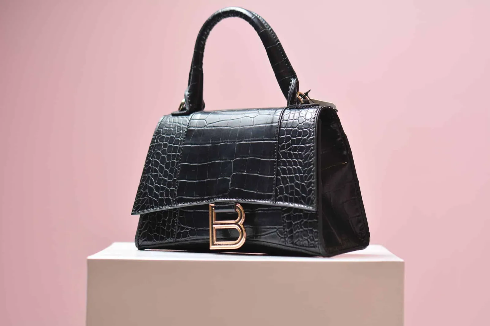 Elegant black leather handbag with textured design on a pink background, perfect for high-end fashion shoots.