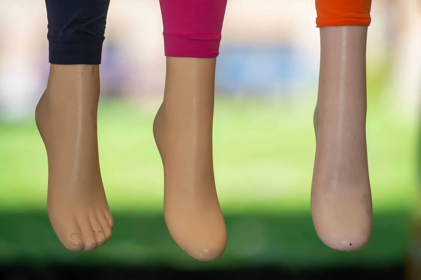 Close-up of mannequin feet in blue, pink, and orange leggings against a green background.