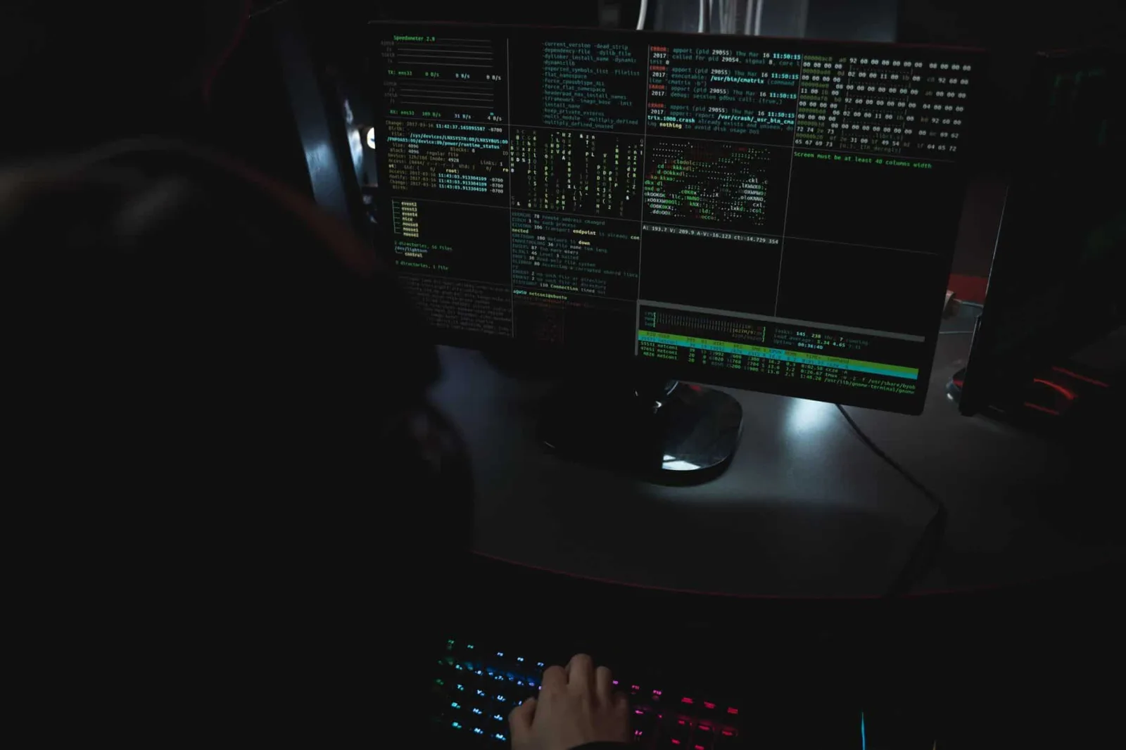 Dark room setup with code displayed on PC monitors highlighting cybersecurity themes.
