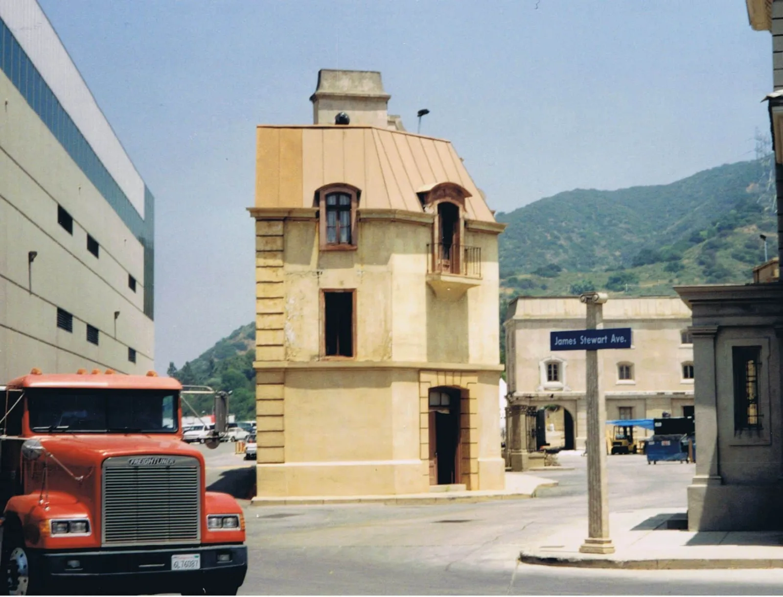 A rustic building on a film studio lot with a parked truck near a mountain background.