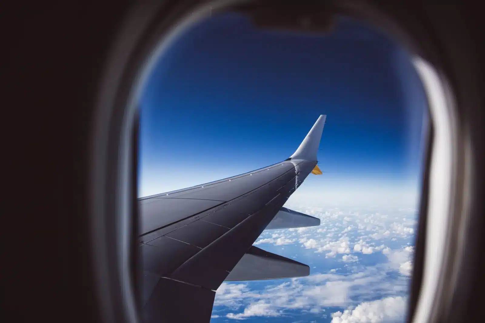 A view from an airplane window showing the wing and clouds below, captured in daylight.